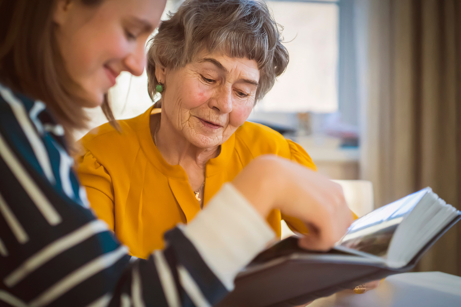 A younger woman and an older woman flipping through a photo album together.